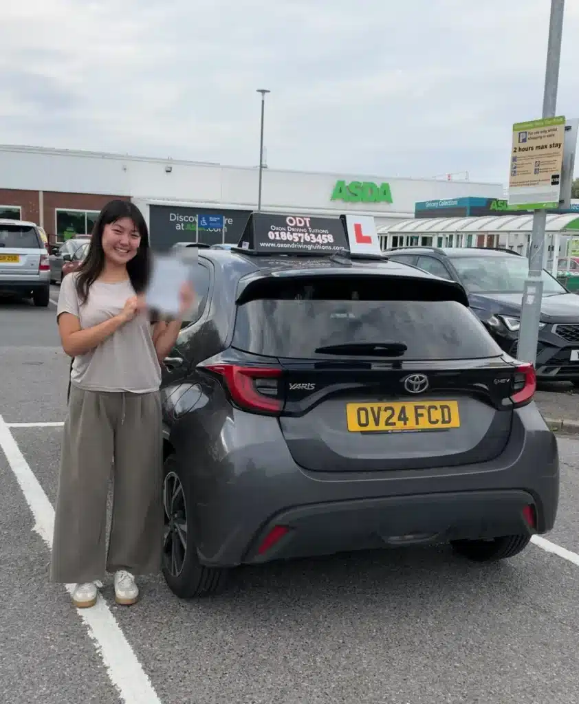 Smiling learner driver holding her pass certificate beside an Oxon Driving Tuitions automatic Toyota Yaris