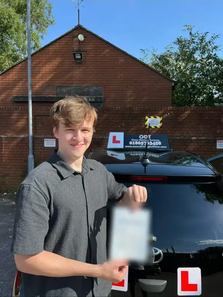 Young learner driver holding up their practical driving test pass certificate behind an Oxon Driving Tuitions car