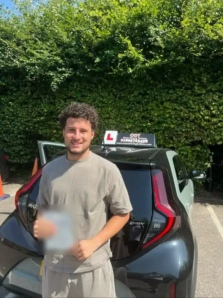 Learner driver holding his pass certificate in front of an Oxon Driving Tuitions automatic Toyota Aygo X