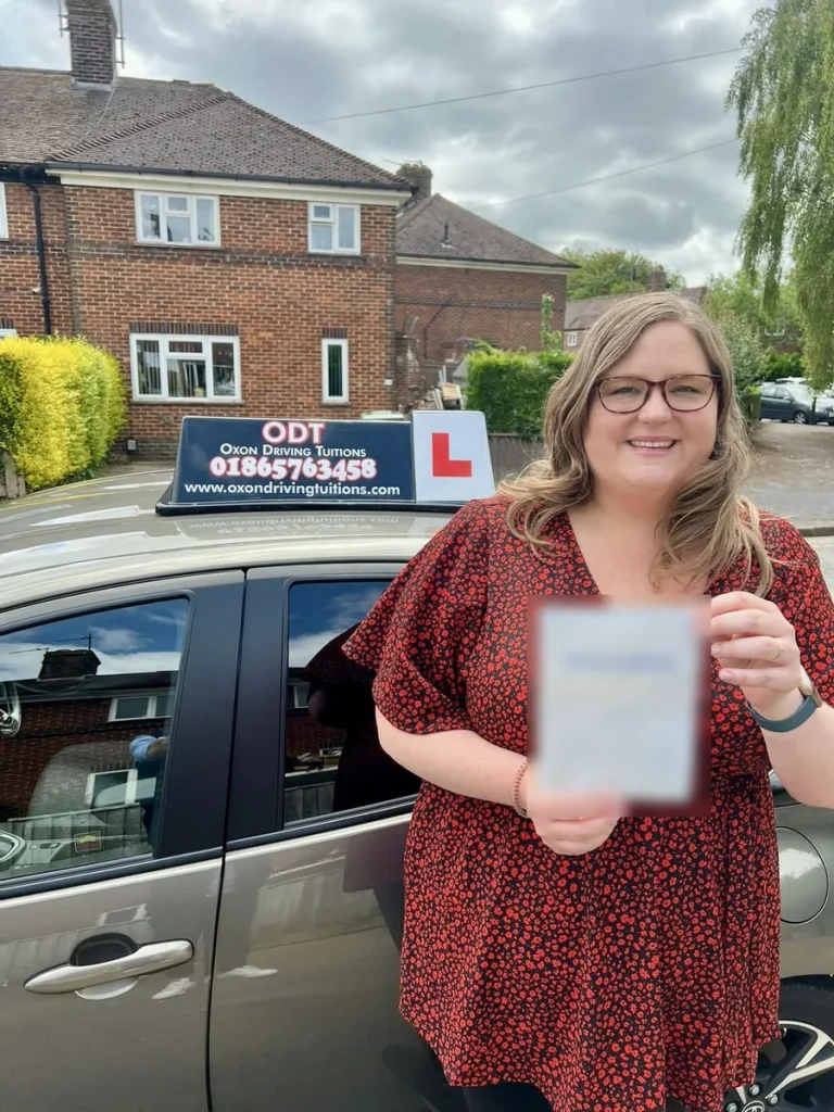 Happy learner driver holding her pass certificate beside an Oxon Driving Tuitions car