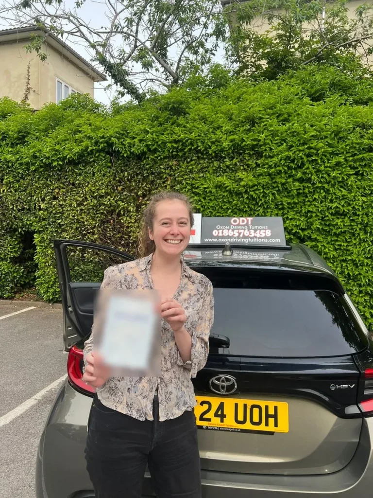 Learner driver smiling with her pass certificate behind an Oxon Driving Tuitions automatic Toyota Yaris