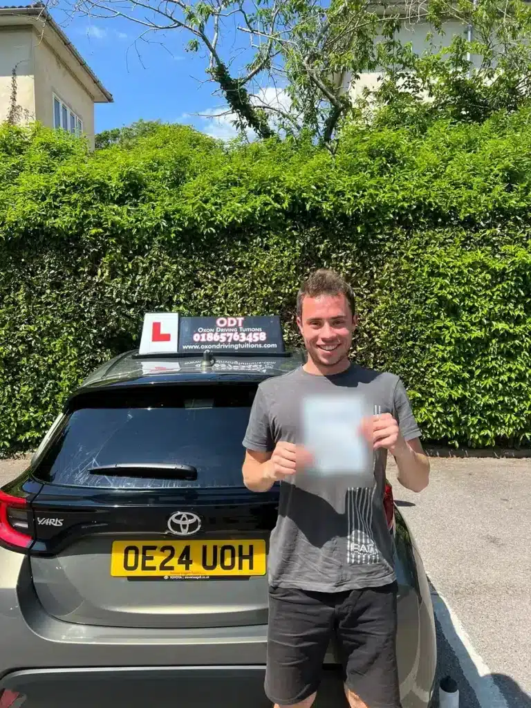 Learner driver holding his pass certificate behind an Oxon Driving Tuitions automatic Toyota Yaris