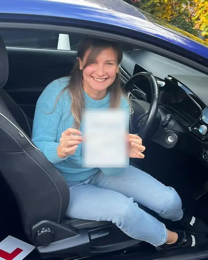 Smiling new driver in the driver seat holding her driving test pass certificate in an Oxon Driving Tuitions car