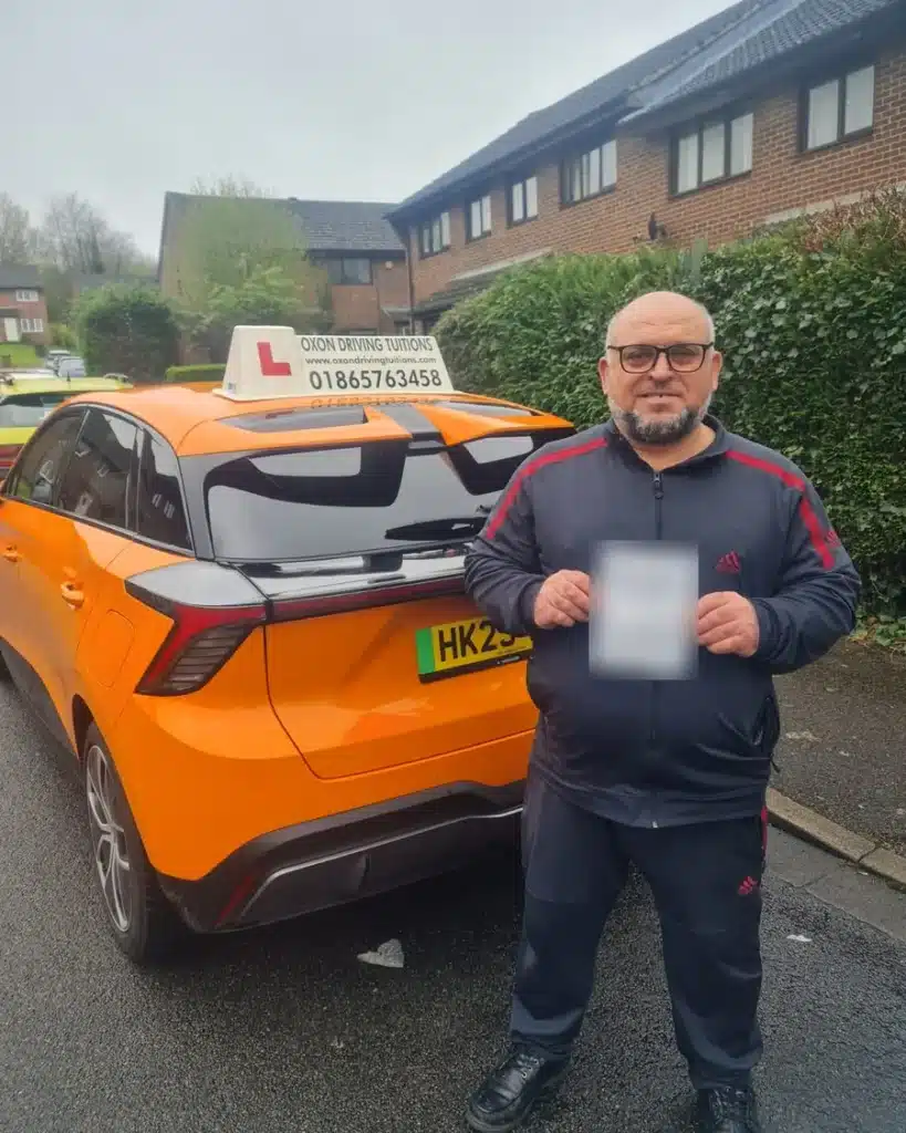 Barton, Headington learner driver holding his driving test pass certificate beside an Oxon Driving Tuitions electric MG4