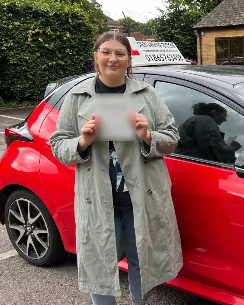 Bicester learner driver holding her driving test pass certificate beside an Oxon Driving Tuitions automatic Toyota Yaris
