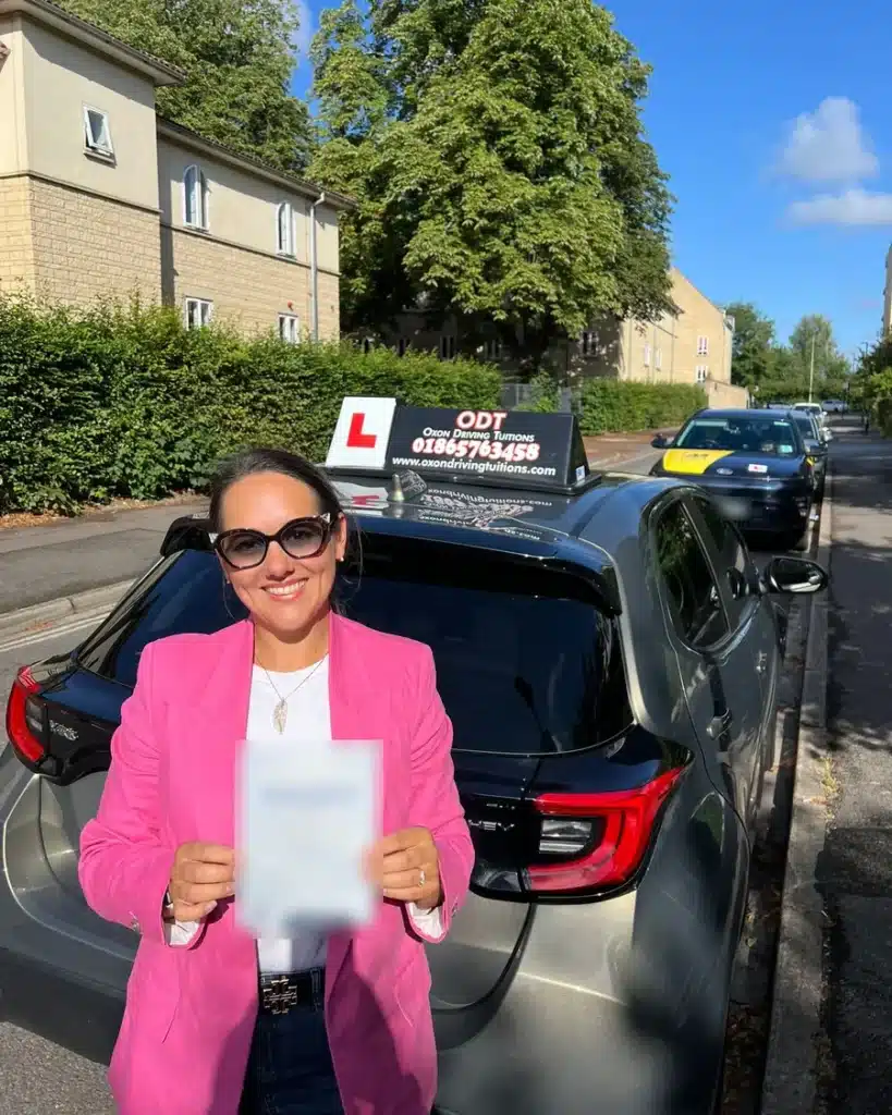 Bicester learner driver smiling with her driving test pass certificate beside an Oxon Driving Tuitions automatic Toyota Yaris