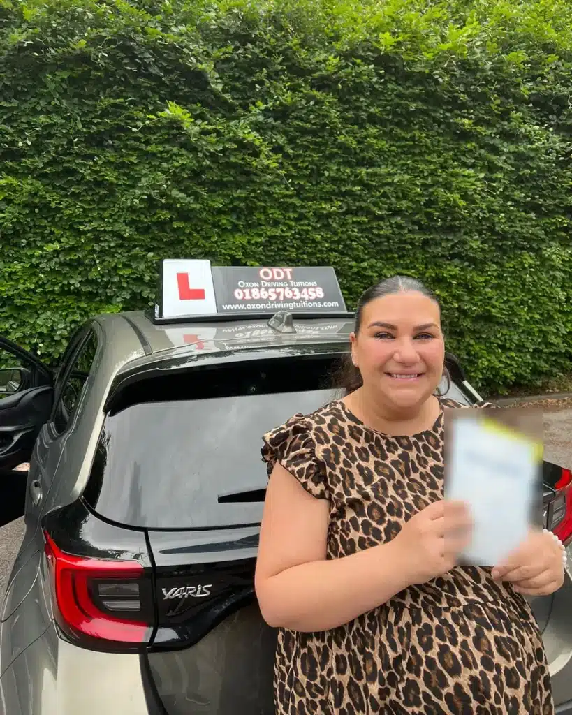 Blackbird Leys learner driver smiling with her driving test pass certificate beside an Oxon Driving Tuitions automatic Toyota Yaris