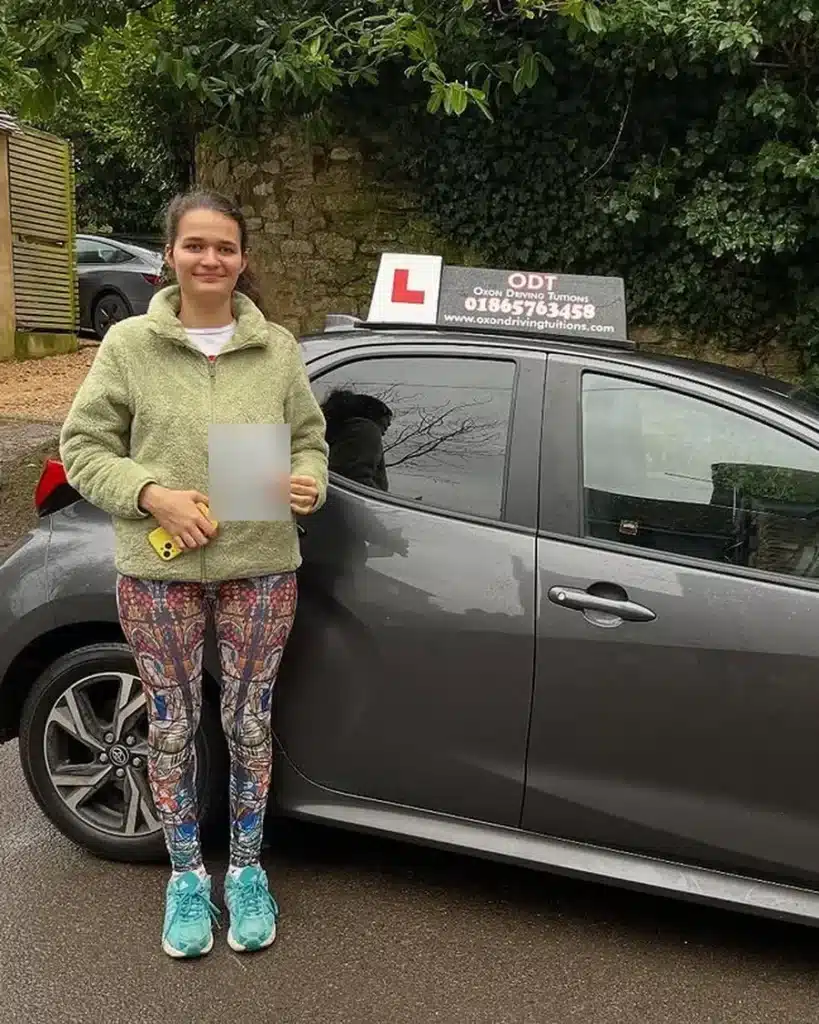 Cassington learner driver holding her driving test pass certificate beside an Oxon Driving Tuitions automatic Toyota Yaris
