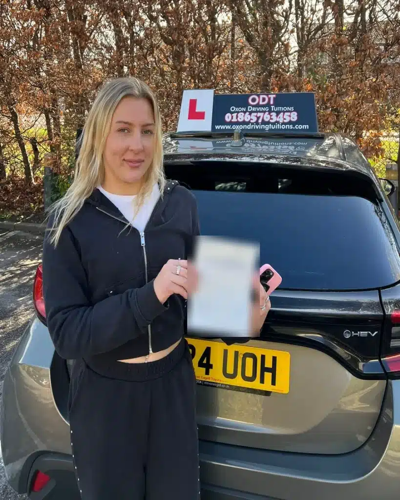 Cowley learner driver holding her driving test pass certificate beside an Oxon Driving Tuitions automatic Toyota Yaris Cross hybrid