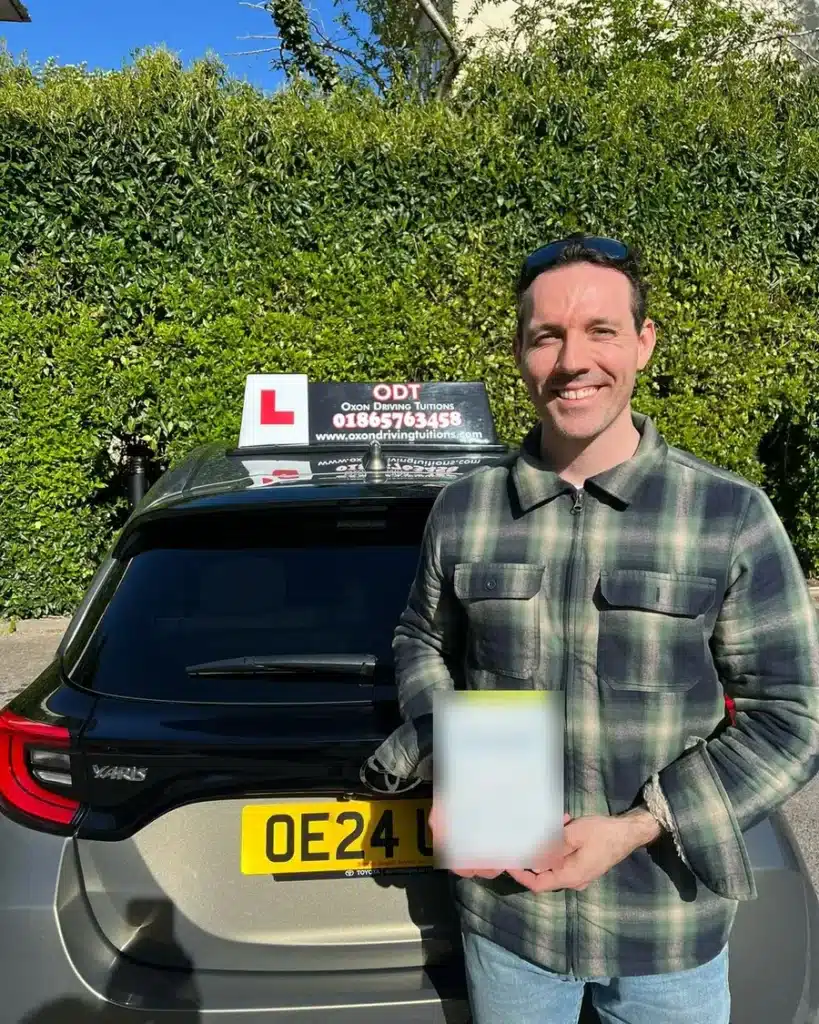 Cutteslowe, North Oxford learner driver smiling with his driving test pass certificate beside an Oxon Driving Tuitions automatic Toyota Yaris