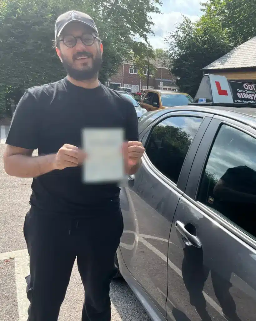 Littlemore learner driver smiling with his driving test pass certificate beside an Oxon Driving Tuitions car
