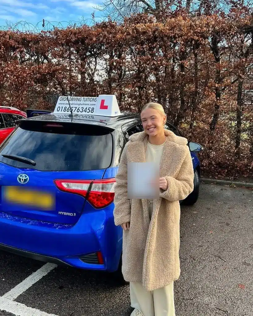 Blackbird Leys learner driver smiling with her driving test pass certificate beside an Oxon Driving Tuitions automatic Toyota Yaris