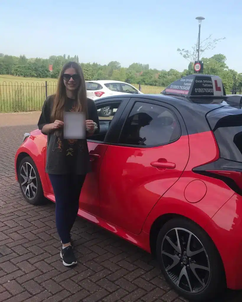 Marston learner driver with her driving test pass certificate beside an Oxon Driving Tuitions automatic Toyota Yaris