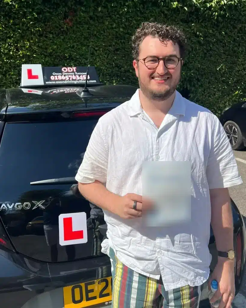 Sandford-on-Thames learner driver smiling with his driving test pass certificate beside an Oxon Driving Tuitions automatic Toyota Aygo X