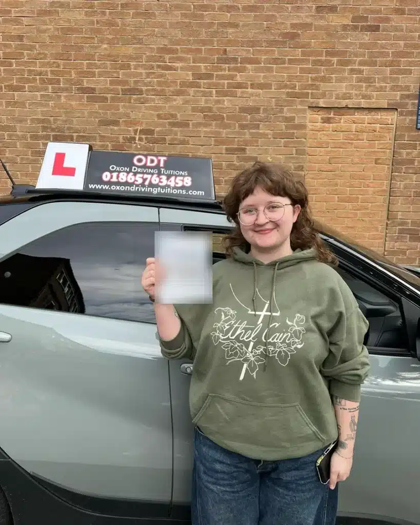 Summertown learner driver smiling with her driving test pass certificate beside an Oxon Driving Tuitions car