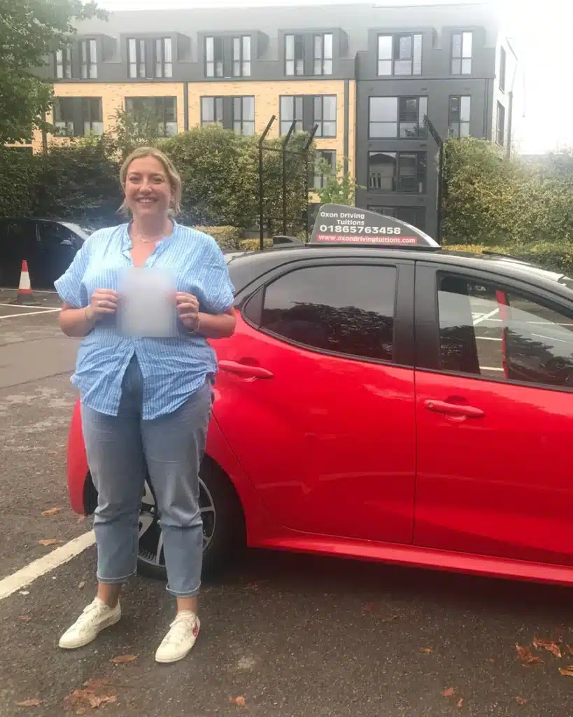 Woodstock Road learner driver smiling with her driving test pass certificate beside an Oxon Driving Tuitions Toyota Yaris