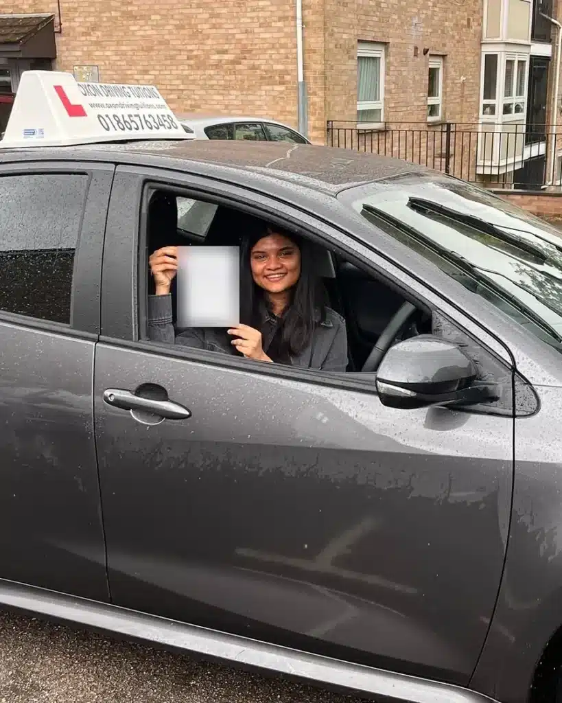 NHS doctor smiling in the driver seat of an Oxon Driving Tuitions car, holding her driving test pass certificate