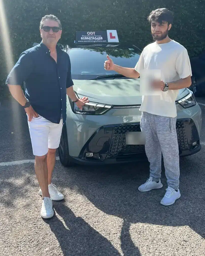 Jan, senior automatic driving instructor at Oxon Driving Tuitions, with a learner holding his pass certificate beside an automatic Toyota Aygo X