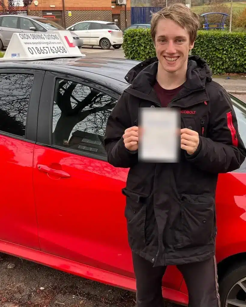 Student learner driver smiling with his driving test pass certificate beside an Oxon Driving Tuitions car